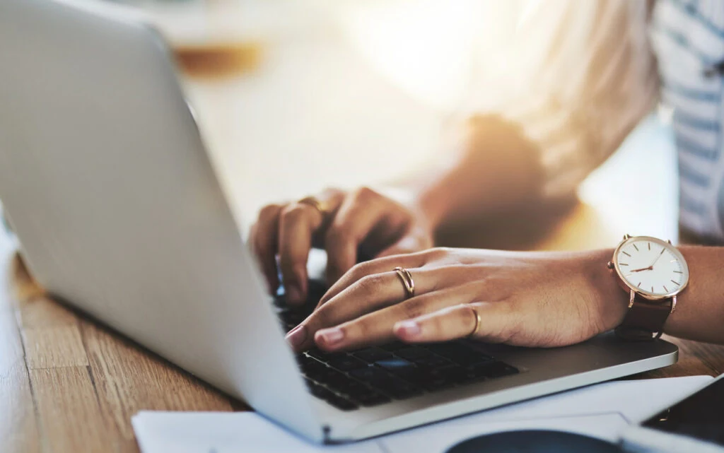 a woman with a ring and watch typing on her laptop